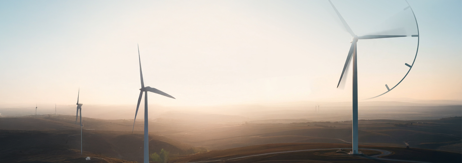 Wide landscape view of a wind farm at sunrise or sunset, with three large wind turbines standing across rolling hills under a hazy sky. The nearest turbine dominates the right side of the image, partially overlaid with a faint clock graphic, suggesting the passage of time or hourly energy matching.